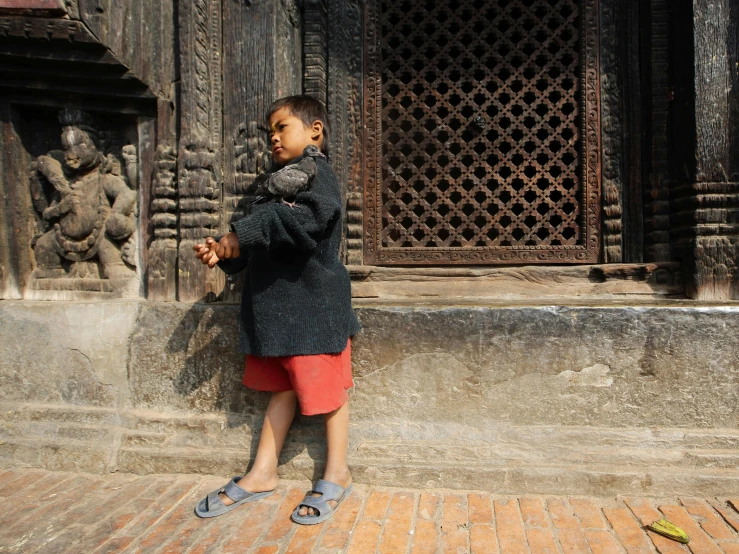 a boy standing by a building with his hand up to the ceiling