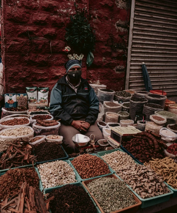 an old man sits among many different colored spices on a market stand