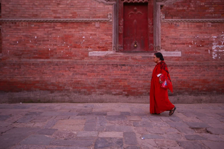 a woman in red coat walking by brick building