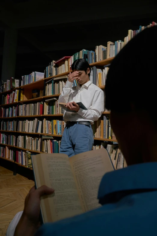 man reading book while wearing formal clothes by bookshelf