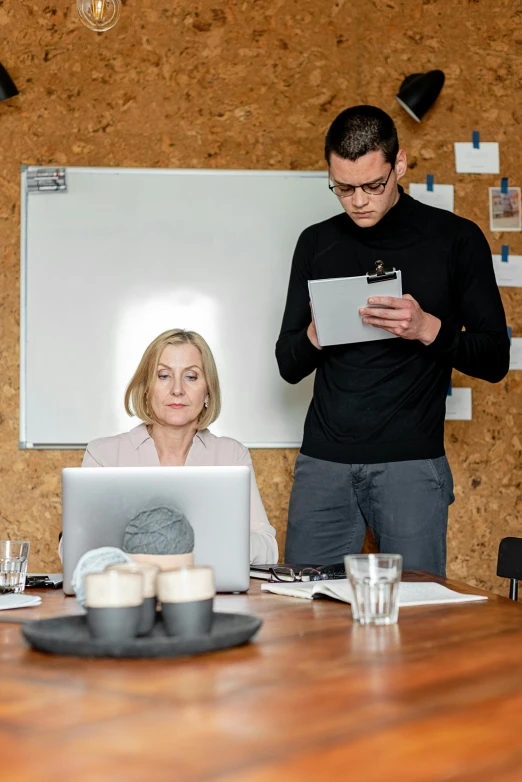 two men and woman are standing around a table looking at a laptop