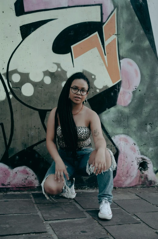 a woman sitting on top of brick pavement next to a wall with graffiti