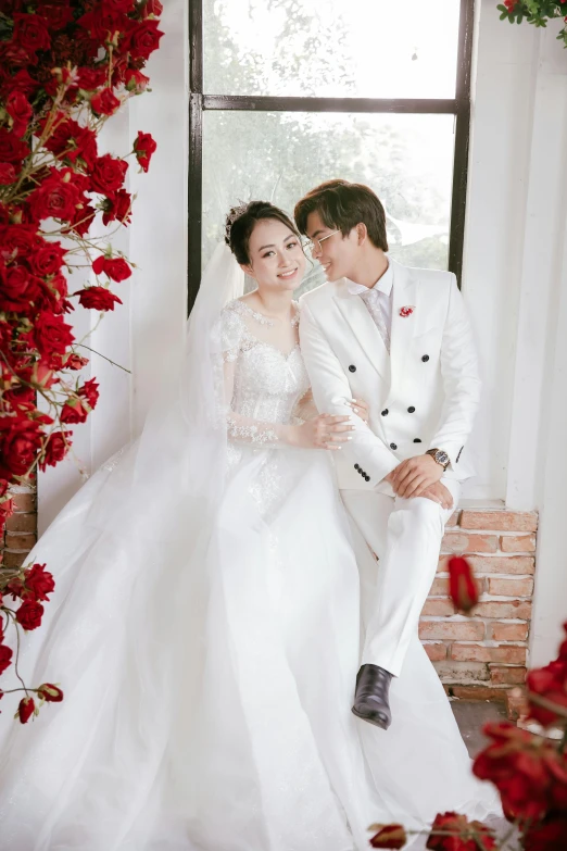 a married couple sits on a brick wall, posing for the camera