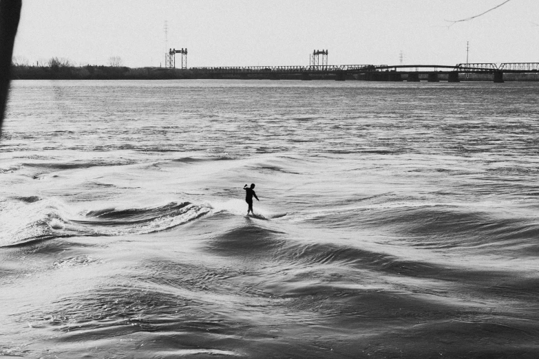 black and white po of person on water next to railroad bridge