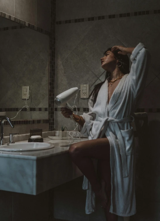 a woman in her bathroom holding a blow dryer while sitting next to a sink