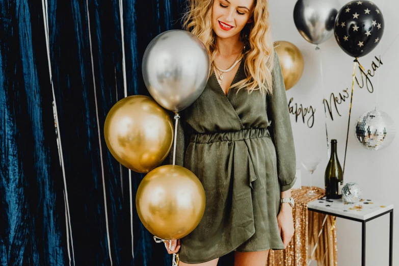 a woman holding a bunch of balloons near a black curtain