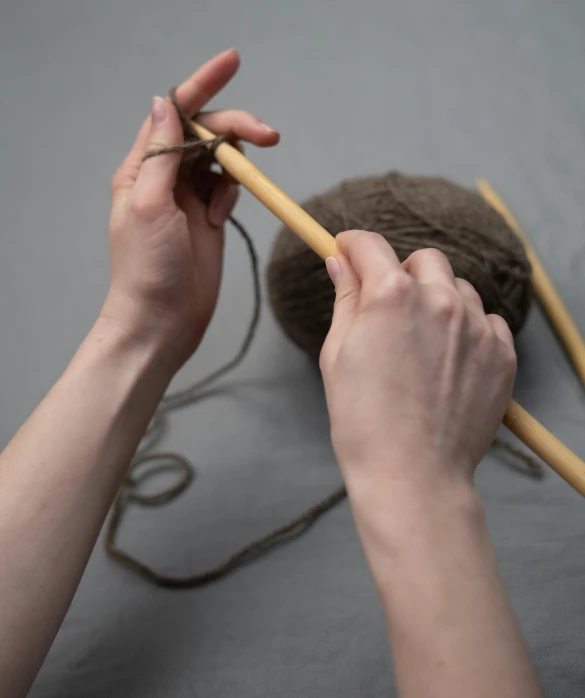 someone knitting a brown ball of yarn with scissors