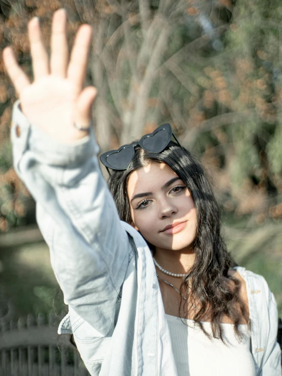 a girl with long hair, sunglasses and a sweater is waving