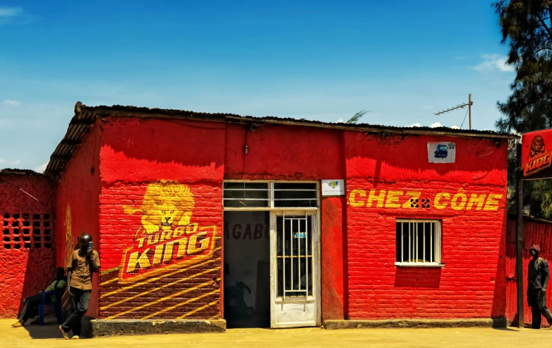 a red building with signs painted on the walls and one man in a hat is walking out the front