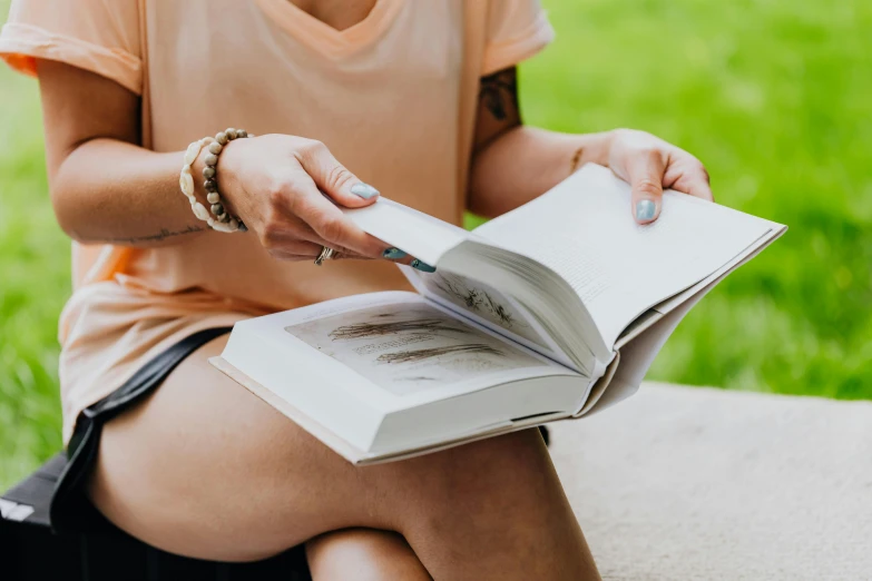 woman in shorts and shirt holding open book outdoors