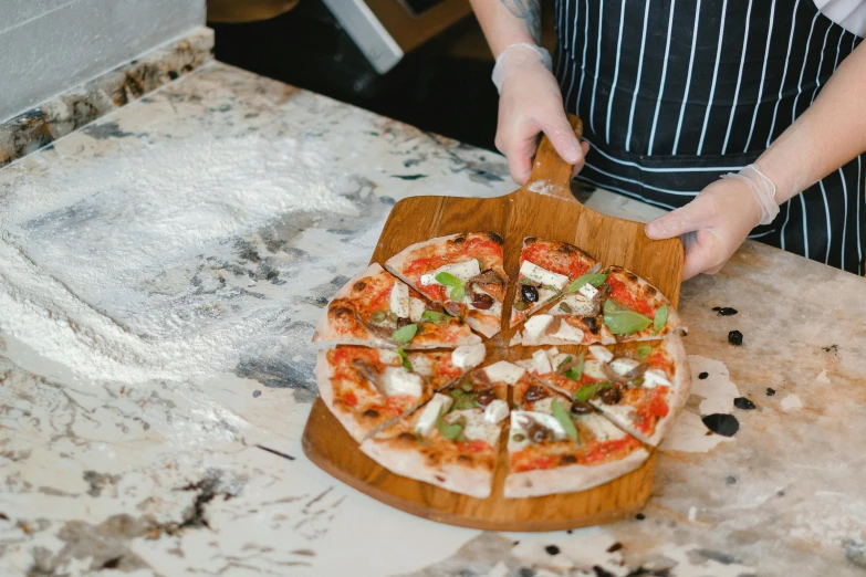 a pizza sits on a wooden board and is being sliced