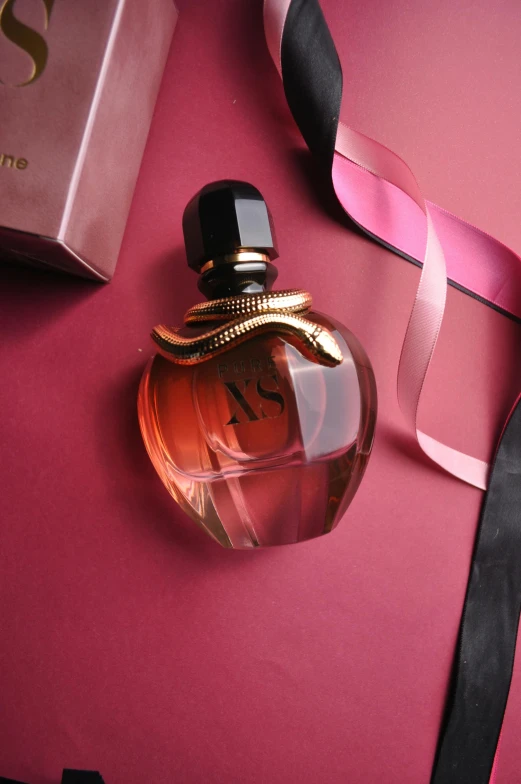 a perfume bottle on a pink surface with ribbons