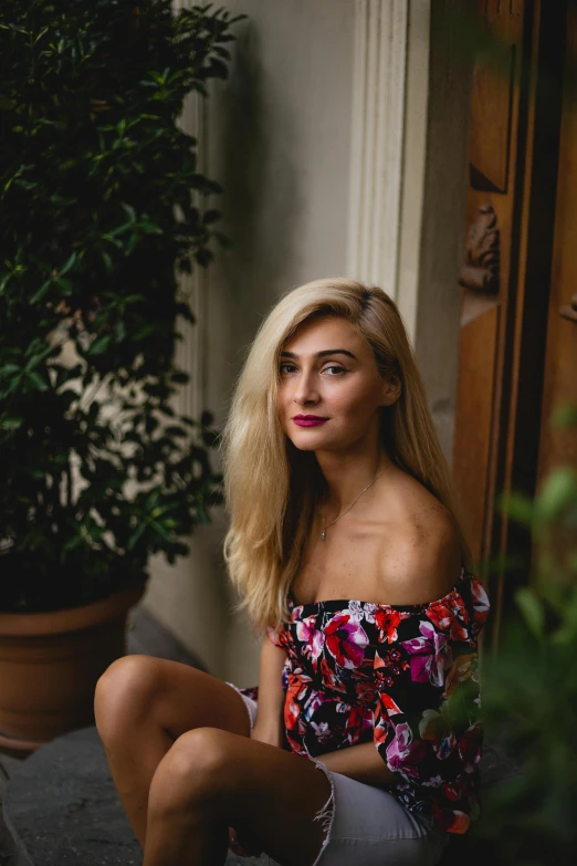 a blonde woman wearing flowers sitting next to potted plants