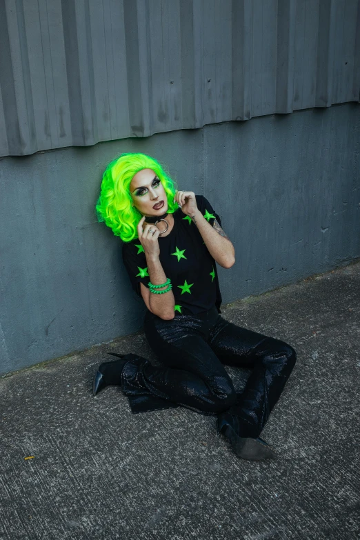 a  wearing a neon green wig, sitting on the pavement