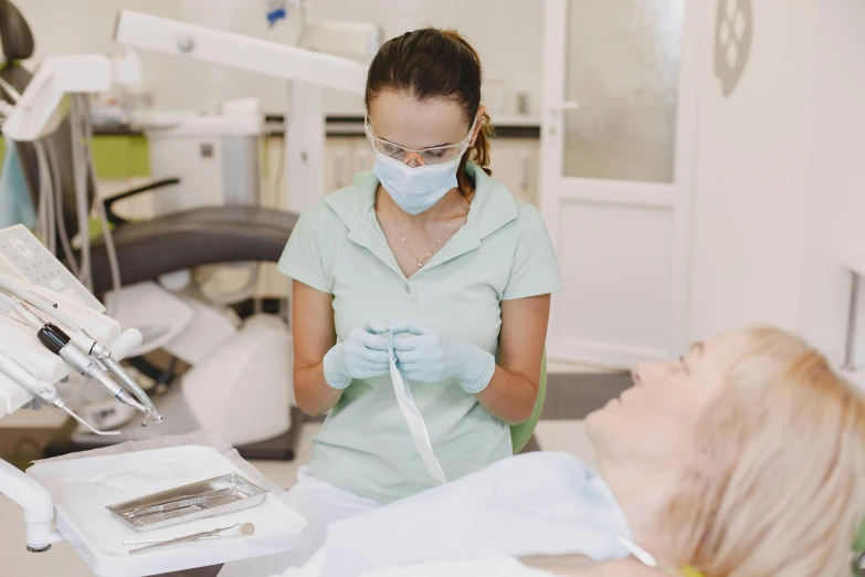 a nurse in a blue scrub suit and a white mask is talking to a woman in a green shirt