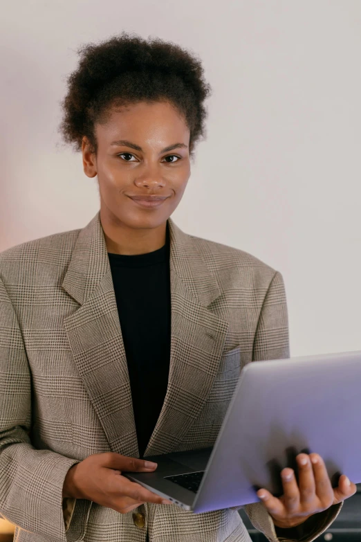 a lady with short hair in a checkered jacket, holds a laptop and looks at the camera