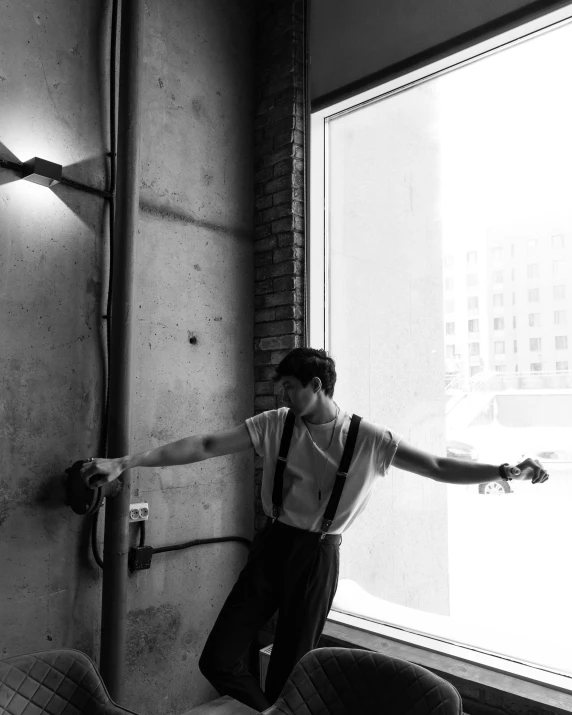 a man wearing suspenders leaning up against a wall next to a window