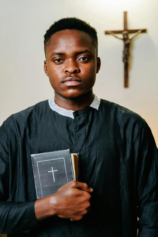 black man wearing a priest's outfit holding a cross and bible