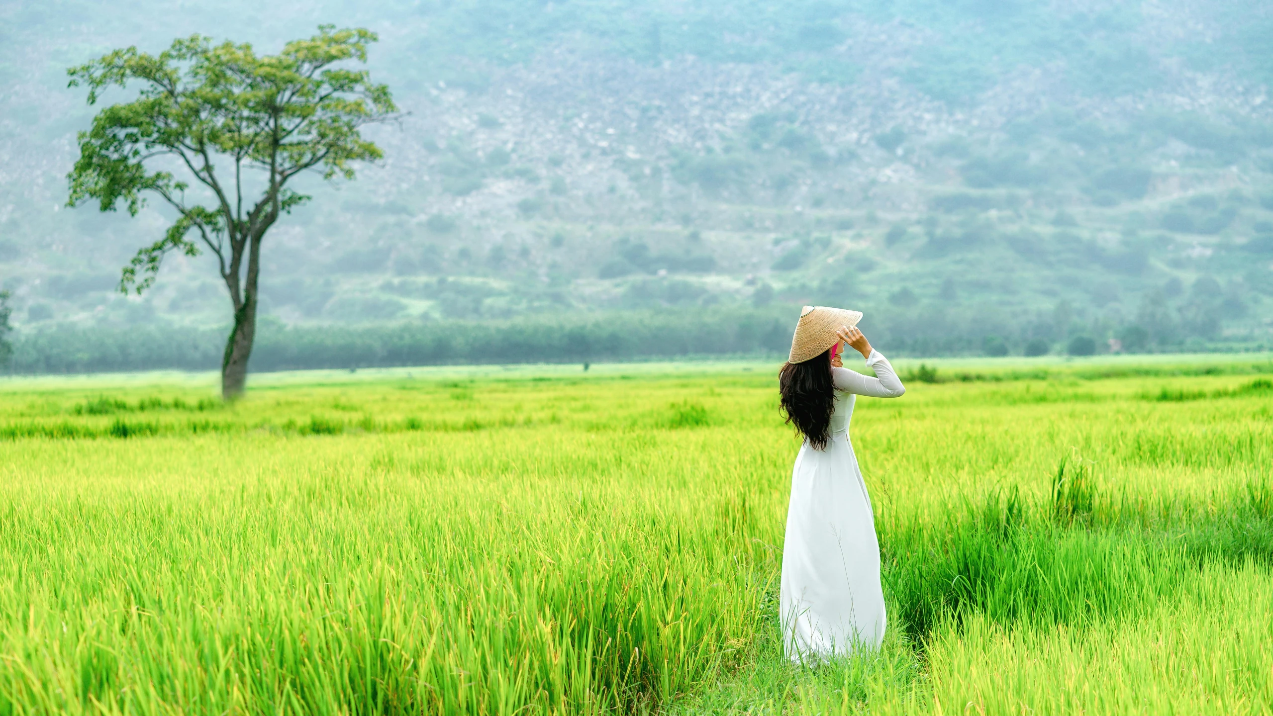 a woman wearing a white dress and hat standing in a field