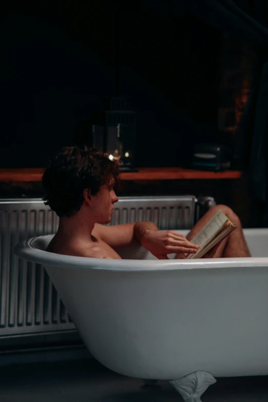 a young man reading a book in a bathtub