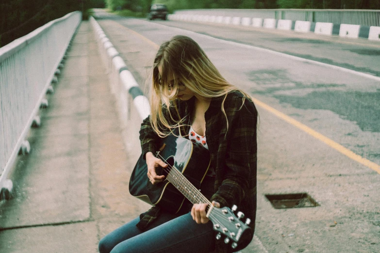 a young woman sitting on the sidewalk playing guitar