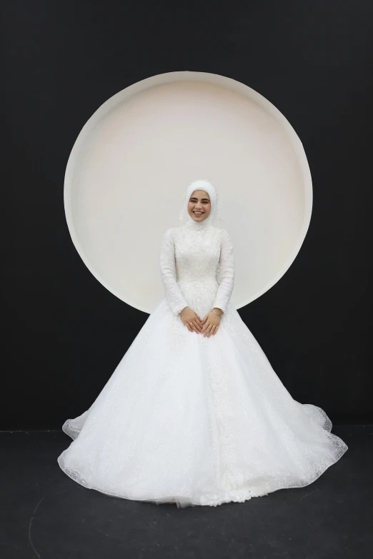 a woman in white gown with a large circular pillow behind her