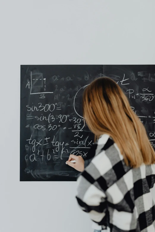 a woman is writing on a black board with writing numbers