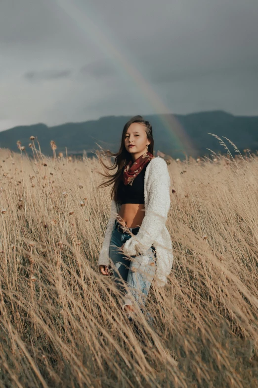 a girl standing in some tall grass with her arm around herself