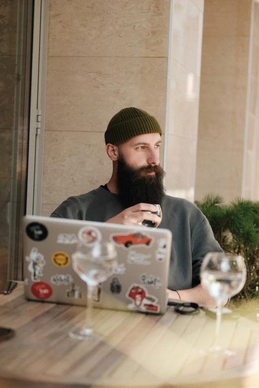 a bearded man sitting at a table using a laptop computer