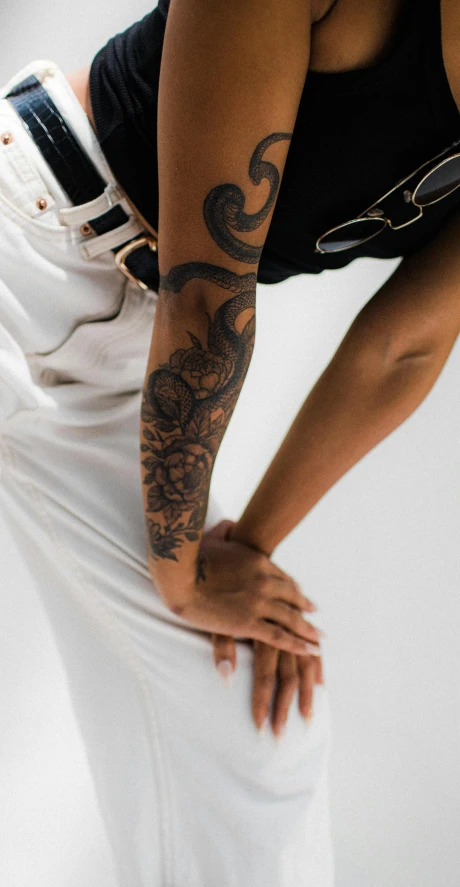 a woman with her hands behind her back, showing off the tattoos on her arm