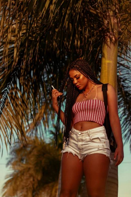 a young woman standing under a palm tree while using her cell phone