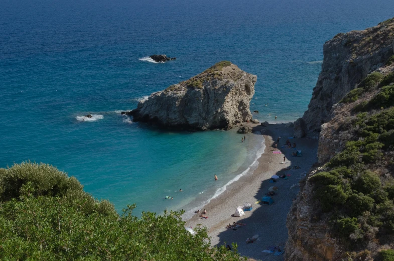 people enjoy the water, sun and sand near a cliff on the sea