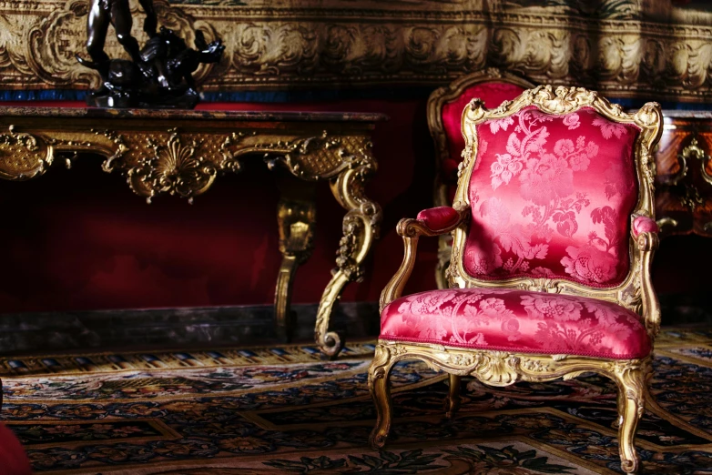 a fancy, gold - plated chair sits next to an ornate wall and table