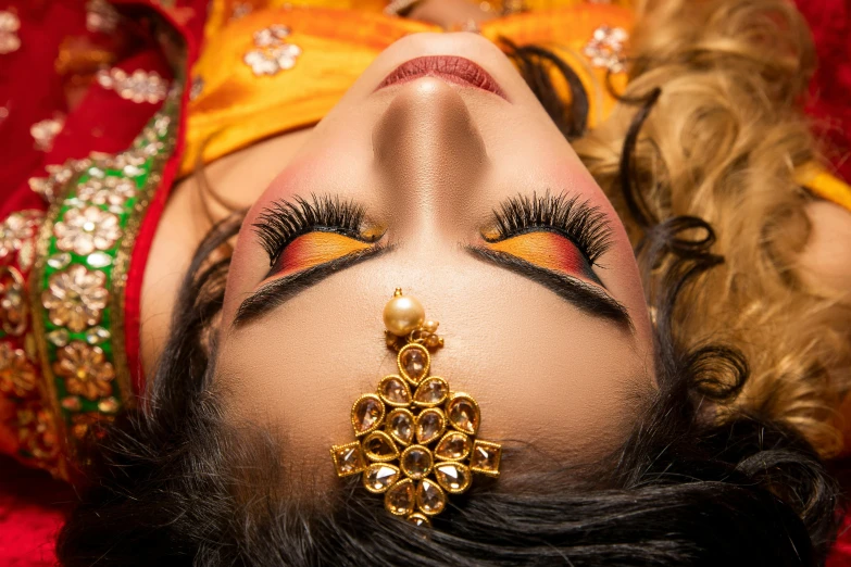 a woman with makeup wearing red and gold with a long bead