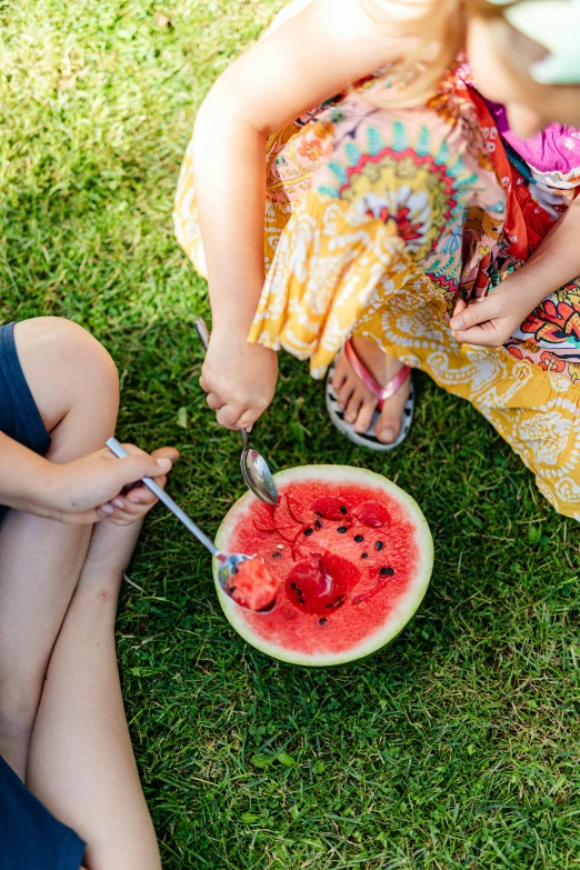 three women sitting around with plates on grass eating food