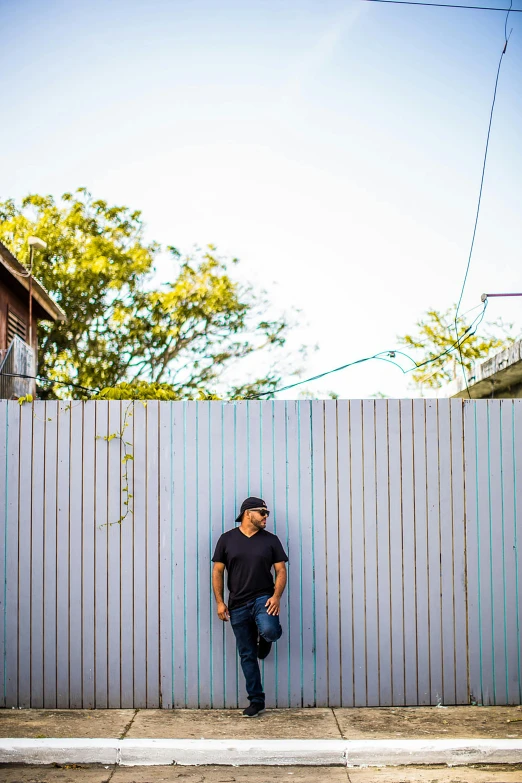 a man is leaning against a fence with his arms in his pockets