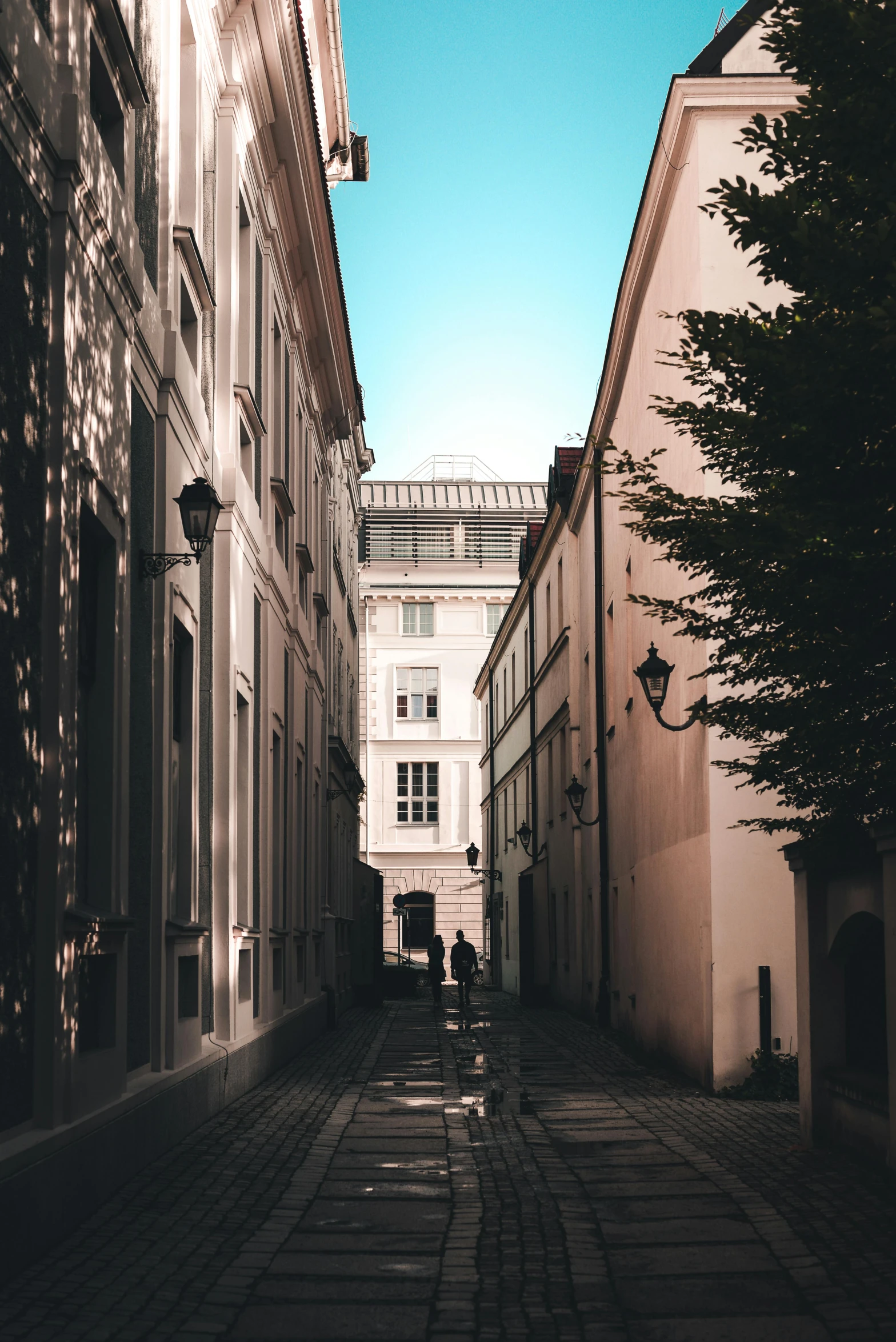 the person standing in the alley between some buildings is taking pos