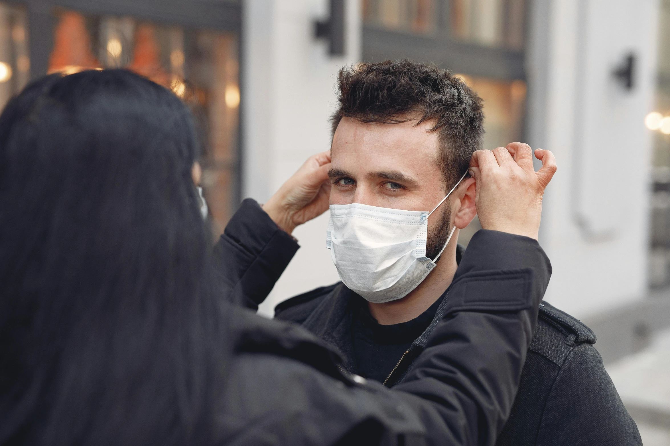 a man in a white mask listens to the ear of a woman wearing a black jacket