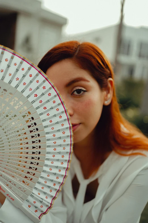 girl with red hair holding fan in open air