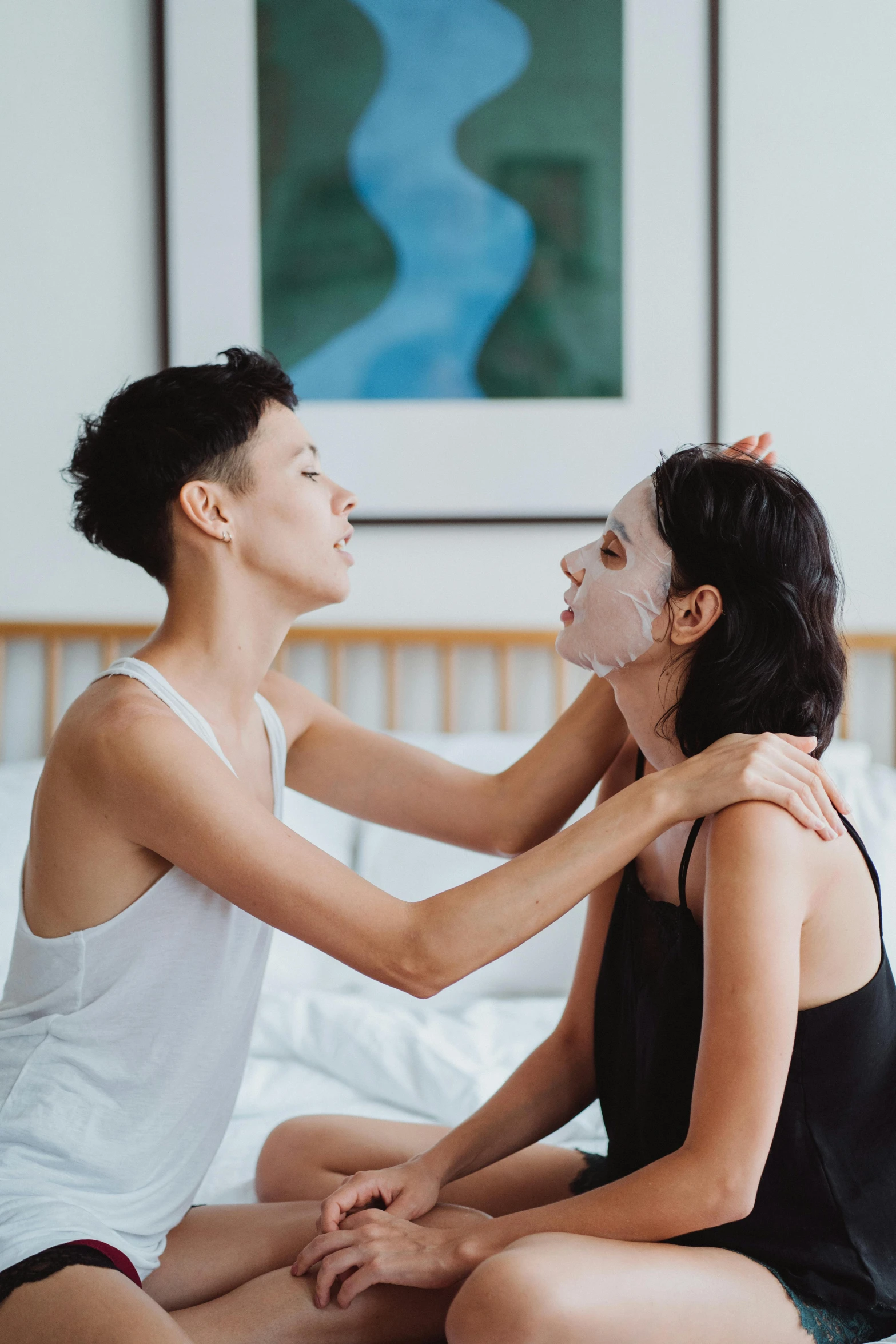 two woman sitting on top of a bed, each touching their face