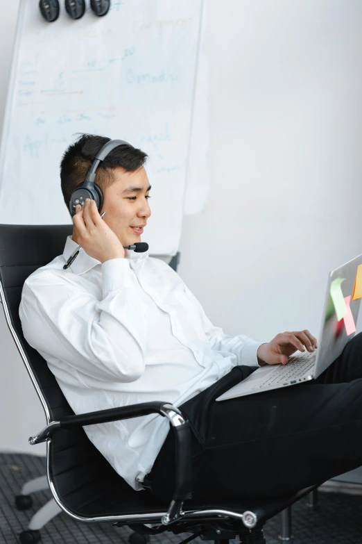 man sitting in chair talking on cell phone and using laptop