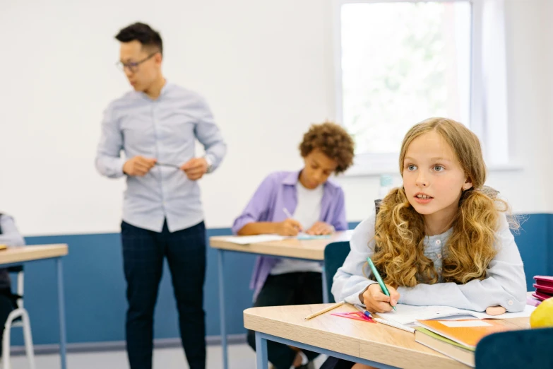 two children are sitting at desks with pens and books in hand