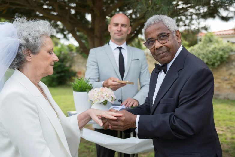 two men are standing outside near one another and one is holding a flower bouquet