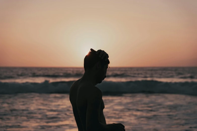 the silhouette of a man with his head up standing at the ocean