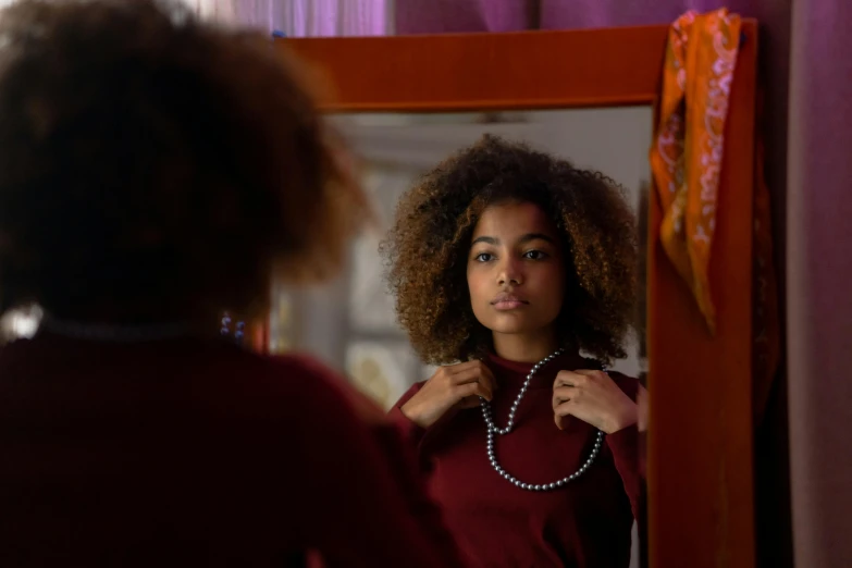 woman looking in mirror while fixing necklace