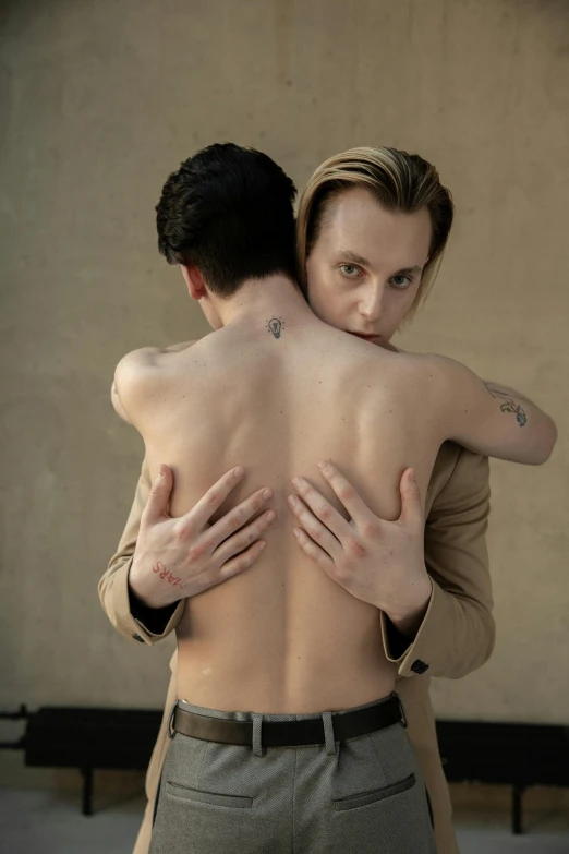 the man is hugging his companion, who also has a large back tattoo