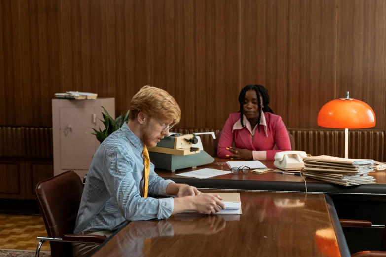 two women sit at a table with paperwork on it