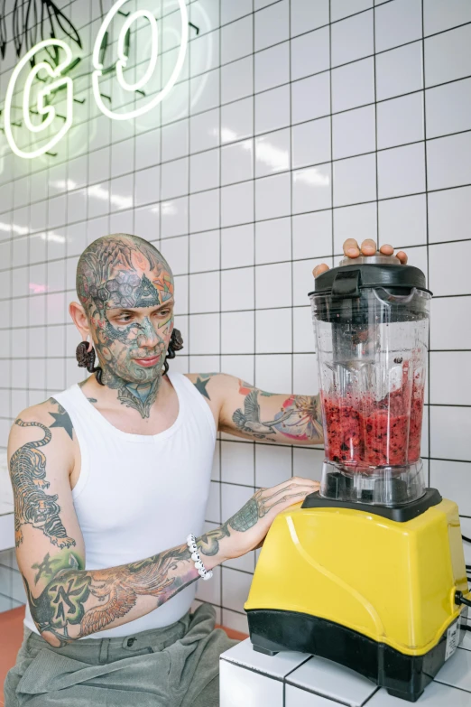 man with tattooed arms standing next to blender