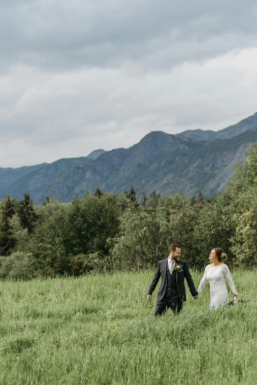 bride and groom walking through grassy area with mountains in background