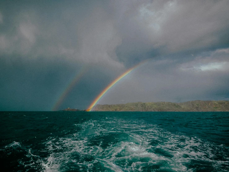 two rainbows shine in the dark clouds over a body of water